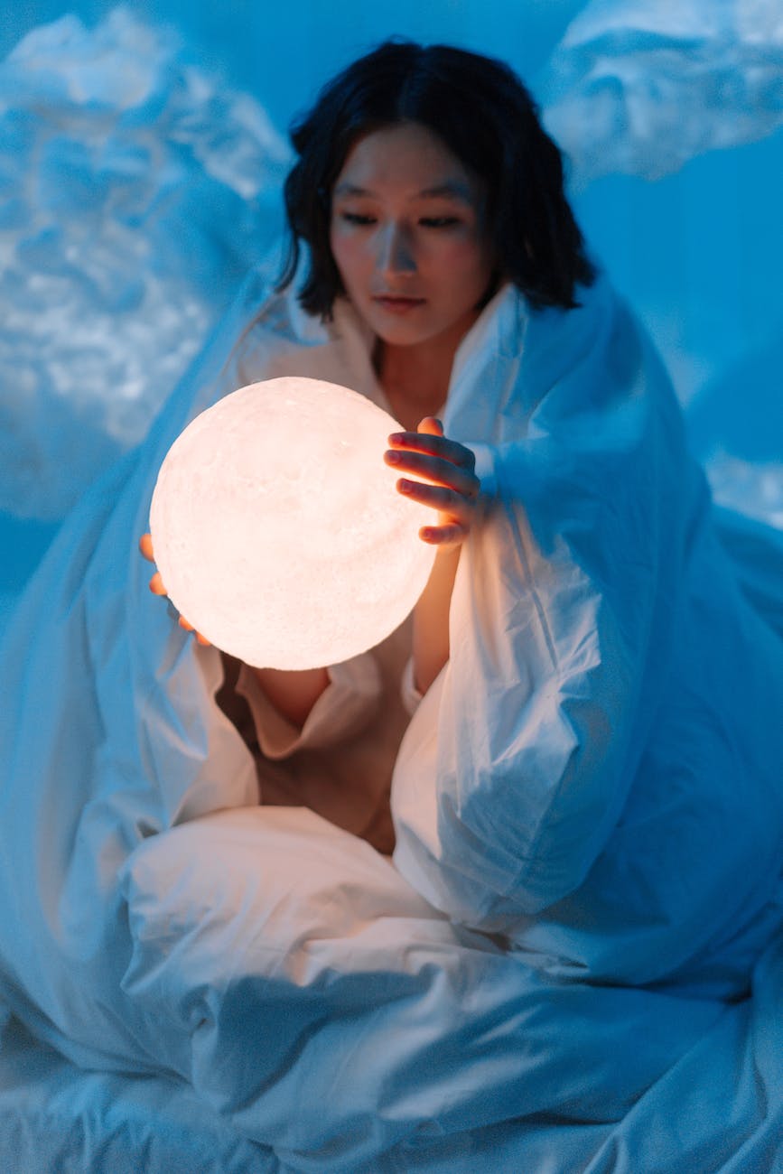 woman in white blanket holding white moon lamp