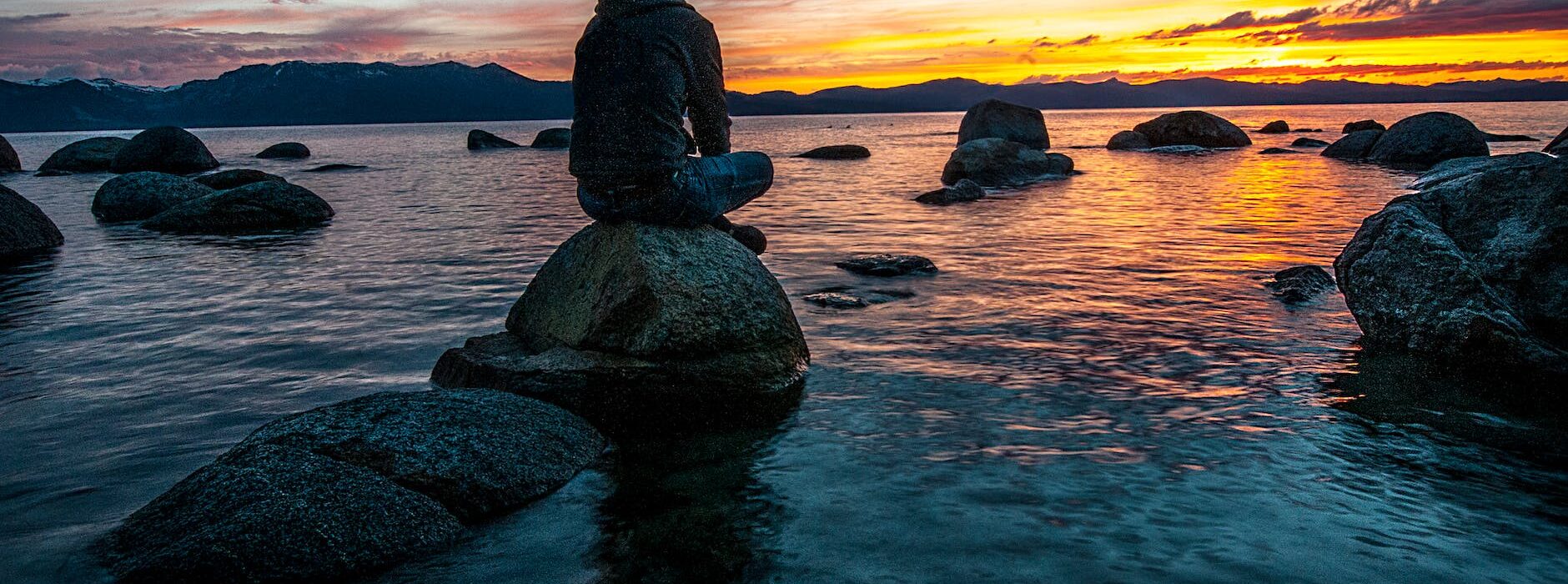person sitting on rock on body of water