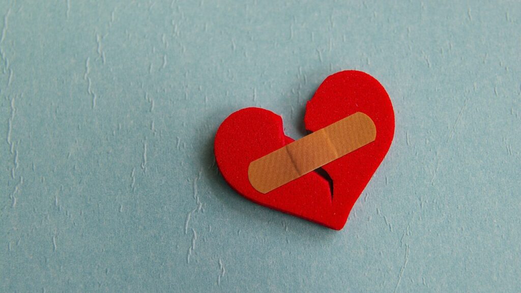 Broken red heart with a bandage on a blue background, representing healing from toxic relationships, trauma bonding, and attachment wounds."